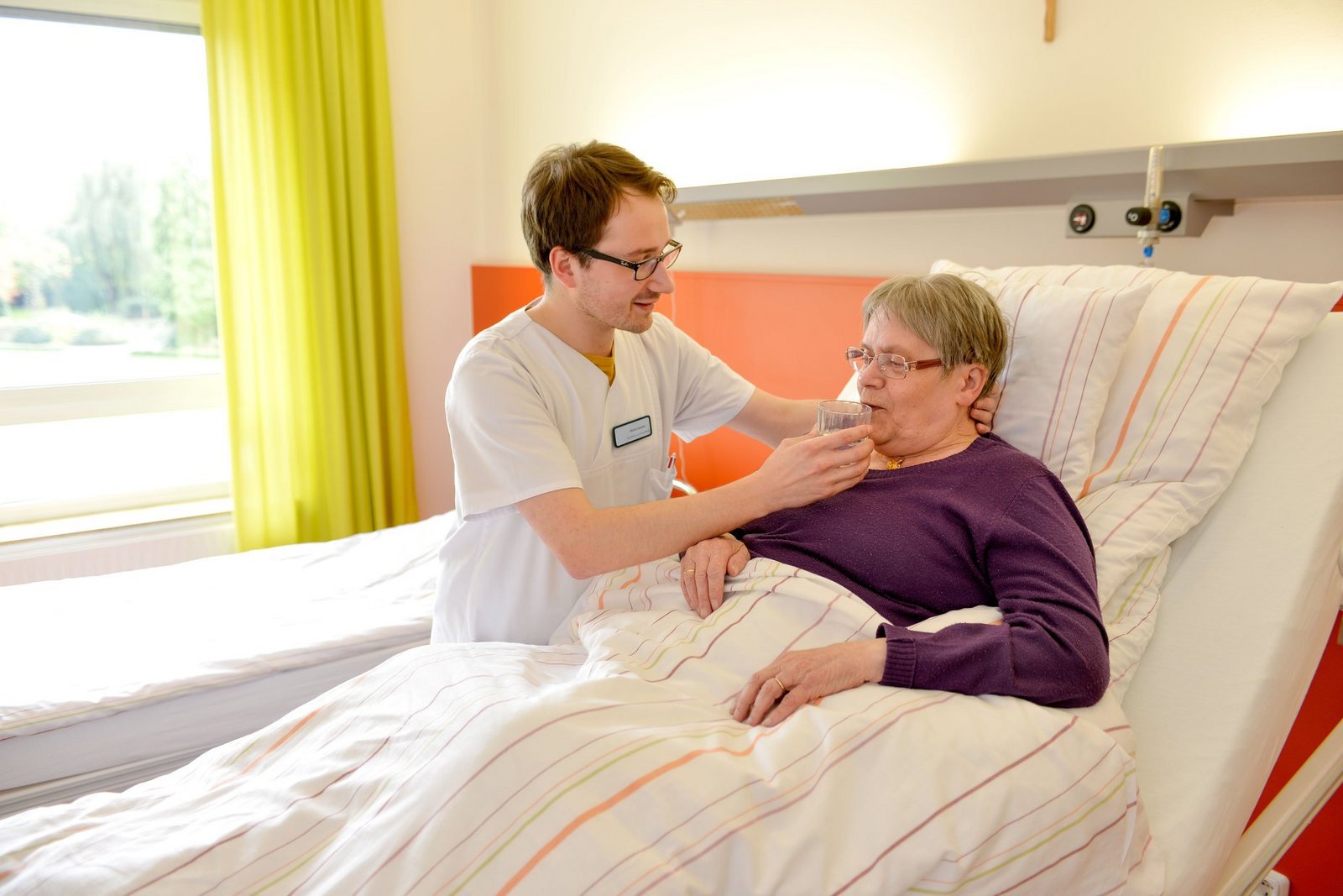 Der Pfleger unterstützt die Patientin beim Trinken